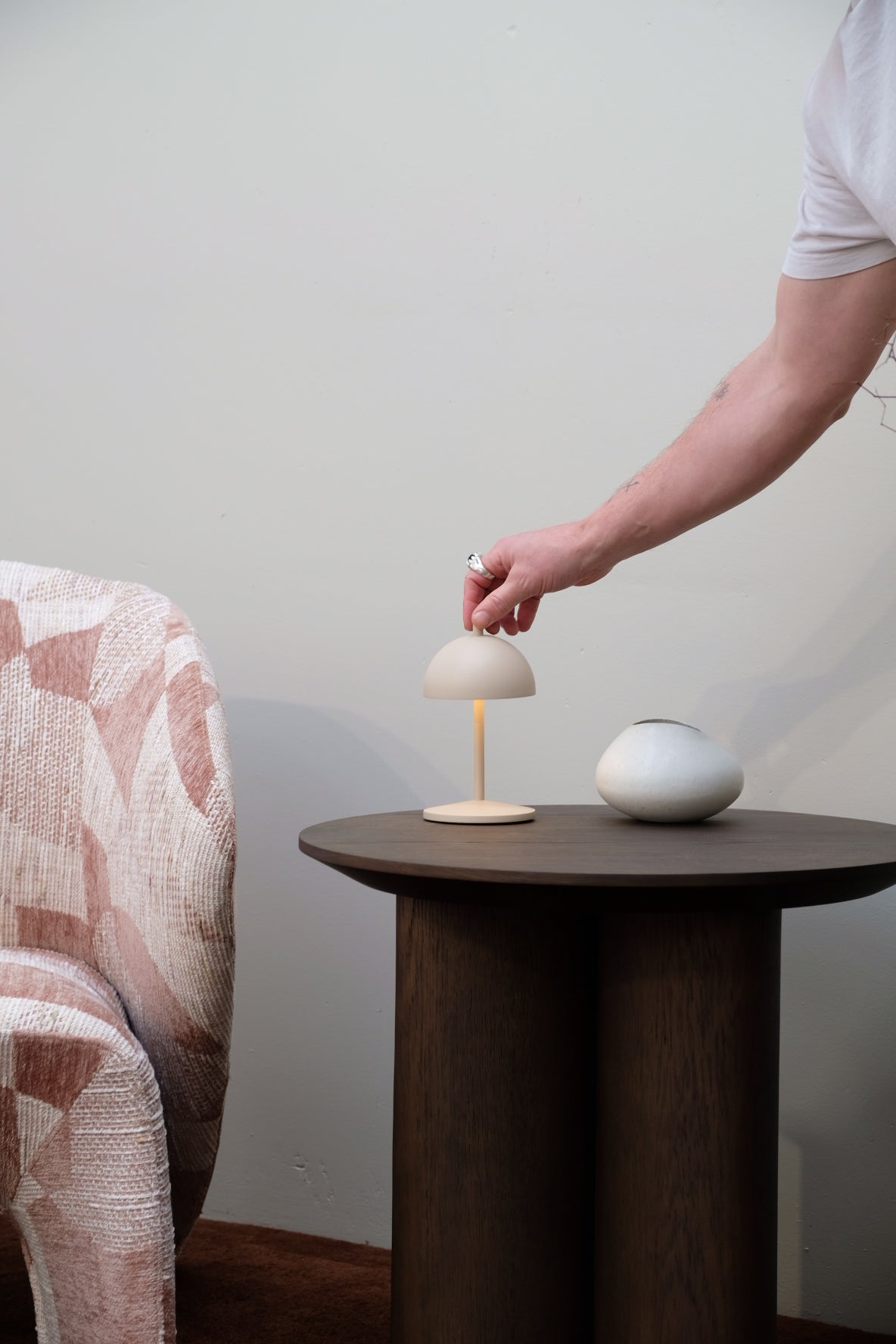 Person adjusting a lamp on a wooden stand against a plain wall
